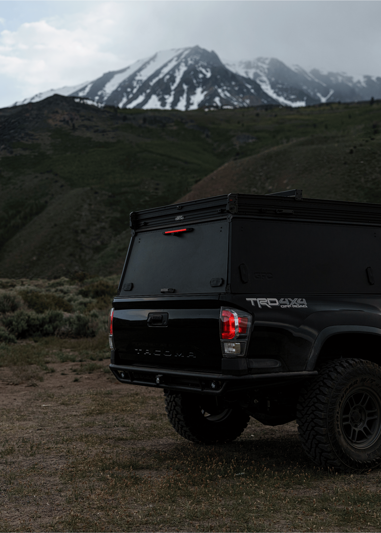 Black Toyota truck with 'TRD Off-Road' badge parked on a dirt road with mountains in the background