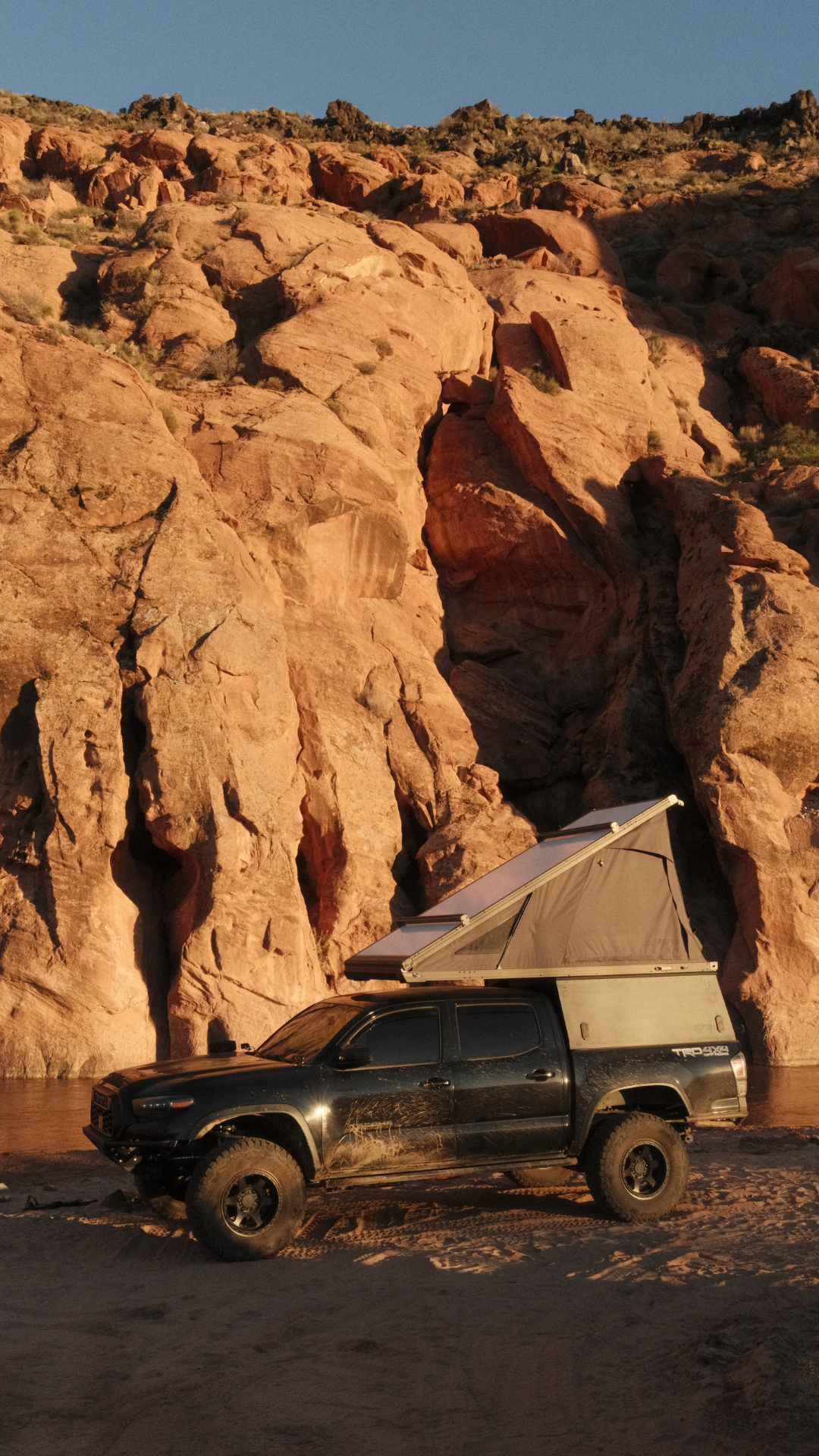 Off-road vehicle with a roof tent parked in front of rocky cliffs
